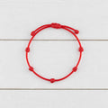 Pulsera de los 7 Nudos en cordón rojo sobre madera blanca