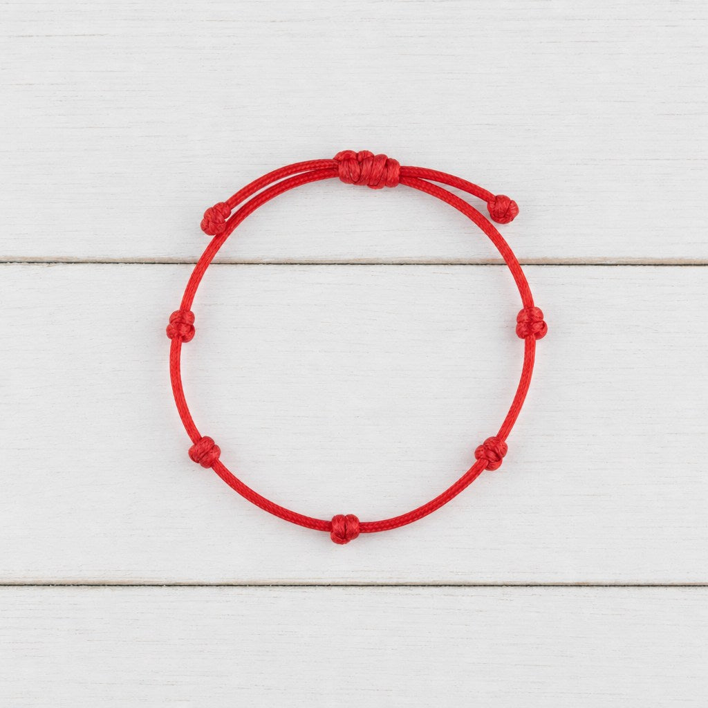 Pulsera de los 7 Nudos en cordón rojo sobre madera blanca